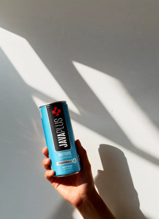 A hand holding a French Vanilla JavaPlus can in raking sunlight
